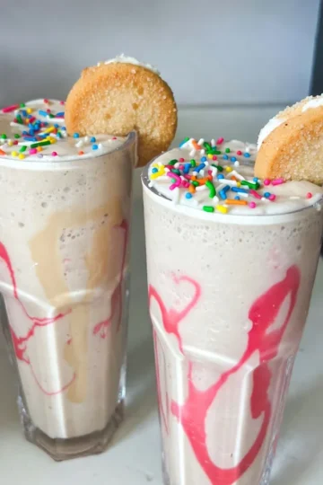 - 1 cup vanilla yogurt - 1 banana, frozen - 1 cup milk (dairy or non-dairy) - 2 tablespoons sugar cookie mix (dry) - 1 teaspoon vanilla extract - 1/2 teaspoon almond extract - 1 tablespoon sprinkles (plus extra for garnish) - Ice cubes (optional) The Frosted Sugar Cookie Smoothie is easy to make and delicious. Each ingredient plays a key role in the flavor and texture. Vanilla yogurt gives a creamy base and a sweet taste. Frozen banana adds a natural sweetness and thickens the smoothie. You can use any milk you like, whether it's cow's milk or a plant-based option. The sugar cookie mix brings that classic cookie flavor right into your drink. For a warm note, add vanilla extract and almond extract. These flavors enhance the sweetness and make the smoothie taste rich. The sprinkles are a fun touch, both in flavor and color. They make the drink feel festive. If you like a thicker smoothie, toss in some ice cubes. They make the drink colder and creamier. Having all these ingredients ready will make your smoothie-making quick and fun! {{ingredient_image_1}} - Step 1: Blend yogurt, banana, and milk First, take your blender and add the vanilla yogurt, frozen banana, and milk. Blend these together until smooth. This mix will be the base of your smoothie. - Step 2: Incorporate sugar cookie mix and extracts Next, add the sugar cookie mix, vanilla extract, and almond extract to the blender. Blend again until everything is mixed well. This step gives your smoothie that sweet cookie flavor. - Step 3: Adjust thickness with ice cubes if desired If you want your smoothie thicker, now is the time to add ice cubes. Blend again until the ice is crushed and fully mixed in. This will make your smoothie cold and refreshing. - Step 4: Add sprinkles for a swirled effect Once your smoothie is smooth, gently stir in the sprinkles. This adds a fun, colorful swirl to your drink, making it look as good as it tastes. - Step 5: Serve in glasses and garnish Pour the smoothie into tall glasses. For a fun finishing touch, sprinkle some extra sprinkles on top. You can even add a small, frosted sugar cookie to the rim of each glass for a special treat. - Use ripe bananas for sweetness: Ripe bananas bring natural sweetness. They make your smoothie taste great without extra sugar. - Selecting the right milk for texture: Choose milk based on your taste. Whole milk gives creaminess, while almond milk adds a light touch. - Tips on using fresh vs. frozen ingredients: Frozen bananas create a thick texture. Fresh bananas can work, but add ice for consistency. - Adding whipped cream as a topping: Whipped cream adds a rich layer. It makes your smoothie look fancy and fun. - Using different types of sprinkles: Choose colorful sprinkles for a pop of joy. You can also try themed sprinkles for special occasions. - Creative glassware suggestions: Serve in tall glasses for an elegant look. You can even use fun cups to make it playful. Pro Tips Use Frozen Bananas: Freezing the bananas not only gives a creamy texture to the smoothie but also keeps it cold and refreshing without needing too much ice. Customize Your Sprinkles: Choose your favorite themed sprinkles for a fun twist, especially for parties or special occasions! Experiment with Milk Alternatives: Try different milk options like almond, oat, or coconut milk for varying flavors and textures in your smoothie. Add a Protein Boost: For an extra nutritional punch, consider adding a scoop of protein powder or a tablespoon of nut butter to your smoothie. {{image_2}} You can change up the flavor of your Frosted Sugar Cookie Smoothie easily. Try using different extracts. For instance, swap the almond extract for coconut or hazelnut. This switch gives your smoothie a fun twist. You can also add new fruits. Strawberries or peaches work great. They add fresh flavors and a nice color. Blend them in with the other ingredients. This makes your smoothie even more unique. Want to make your smoothie vegan? You can do that! Just use plant-based yogurt and milk. Almond, soy, or coconut milk are great choices. These options keep the flavor rich while being dairy-free. If you want to lower the sugar, try using a sugar substitute. Stevia or monk fruit sweetener can work well. This way, you can enjoy your smoothie without too much sugar. Store any leftover Frosted Sugar Cookie Smoothie in the fridge. Use a sealed container to keep it fresh. It is best to drink the smoothie within one day. The yogurt and banana may change texture over time. If you want to freeze it, pour the smoothie into ice cube trays. This way, you can use it later in other smoothies. Just blend the frozen cubes with a little milk when you want a quick treat. If you have leftover smoothie, here's how to revive it. Pour it back into the blender. Blend it again to mix. If it is too thick, add a little milk. This helps keep the texture smooth. Taste it after blending. If it needs more flavor, add a drop of vanilla or a sprinkle of sugar cookie mix. Enjoy your smoothie just like it was fresh! Can I use regular cookies instead of cookie mix? Yes, you can use regular sugar cookies. Just crush them into small bits. This will give your smoothie a nice texture. Use about two cookies per smoothie. How long does the smoothie last in the fridge? The smoothie stays fresh for about one day in the fridge. After that, it may lose its taste and texture. Be sure to store it in a sealed container to keep it fresh. Is it possible to make this smoothie without a blender? You can make this smoothie without a blender, but it will be harder. Try using a whisk or a fork to mix the ingredients. This method works best for small batches. What can I add to enhance the nutritional value? You can add spinach or kale for extra vitamins. Greek yogurt adds protein, while chia seeds boost fiber. Nuts or seeds can also add healthy fats and crunch. This smoothie combines simple ingredients for a tasty treat. You blend yogurt, banana, and milk, then add sugar cookie mix and extracts. Adjust the thickness with ice cubes, and don’t forget the sprinkles. You can customize flavors and even make it vegan. Store leftovers in the fridge or freeze for later. Enjoy this fun, easy drink whenever you crave something sweet and refreshing!