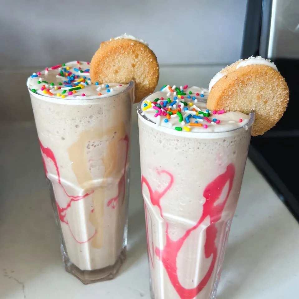 - 1 cup vanilla yogurt - 1 banana, frozen - 1 cup milk (dairy or non-dairy) - 2 tablespoons sugar cookie mix (dry) - 1 teaspoon vanilla extract - ½ teaspoon almond extract - 1 tablespoon sprinkles (plus extra for garnish) - Ice cubes (optional) The Frosted Sugar Cookie Smoothie is easy to make and delicious. Each ingredient plays a key role in the flavor and texture. Vanilla yogurt gives a creamy base and a sweet taste. Frozen banana adds a natural sweetness and thickens the smoothie. You can use any milk you like, whether it's cow's milk or a plant-based option. The sugar cookie mix brings that classic cookie flavor right into your drink. For a warm note, add vanilla extract and almond extract. These flavors enhance the sweetness and make the smoothie taste rich. The sprinkles are a fun touch, both in flavor and color. They make the drink feel festive. If you like a thicker smoothie, toss in some ice cubes. They make the drink colder and creamier. Having all these ingredients ready will make your smoothie-making quick and fun! {{ingredient_image_1}} - Step 1: Blend yogurt, banana, and milk First, take your blender and add the vanilla yogurt, frozen banana, and milk. Blend these together until smooth. This mix will be the base of your smoothie. - Step 2: Incorporate sugar cookie mix and extracts Next, add the sugar cookie mix, vanilla extract, and almond extract to the blender. Blend again until everything is mixed well. This step gives your smoothie that sweet cookie flavor. - Step 3: Adjust thickness with ice cubes if desired If you want your smoothie thicker, now is the time to add ice cubes. Blend again until the ice is crushed and fully mixed in. This will make your smoothie cold and refreshing. - Step 4: Add sprinkles for a swirled effect Once your smoothie is smooth, gently stir in the sprinkles. This adds a fun, colorful swirl to your drink, making it look as good as it tastes. - Step 5: Serve in glasses and garnish Pour the smoothie into tall glasses. For a fun finishing touch, sprinkle some extra sprinkles on top. You can even add a small, frosted sugar cookie to the rim of each glass for a special treat. - Use ripe bananas for sweetness: Ripe bananas bring natural sweetness. They make your smoothie taste great without extra sugar. - Selecting the right milk for texture: Choose milk based on your taste. Whole milk gives creaminess, while almond milk adds a light touch. - Tips on using fresh vs. frozen ingredients: Frozen bananas create a thick texture. Fresh bananas can work, but add ice for consistency. - Adding whipped cream as a topping: Whipped cream adds a rich layer. It makes your smoothie look fancy and fun. - Using different types of sprinkles: Choose colorful sprinkles for a pop of joy. You can also try themed sprinkles for special occasions. - Creative glassware suggestions: Serve in tall glasses for an elegant look. You can even use fun cups to make it playful. Pro Tips Use Frozen Bananas: Freezing the bananas not only gives a creamy texture to the smoothie but also keeps it cold and refreshing without needing too much ice. Customize Your Sprinkles: Choose your favorite themed sprinkles for a fun twist, especially for parties or special occasions! Experiment with Milk Alternatives: Try different milk options like almond, oat, or coconut milk for varying flavors and textures in your smoothie. Add a Protein Boost: For an extra nutritional punch, consider adding a scoop of protein powder or a tablespoon of nut butter to your smoothie. {{image_2}} You can change up the flavor of your Frosted Sugar Cookie Smoothie easily. Try using different extracts. For instance, swap the almond extract for coconut or hazelnut. This switch gives your smoothie a fun twist. You can also add new fruits. Strawberries or peaches work great. They add fresh flavors and a nice color. Blend them in with the other ingredients. This makes your smoothie even more unique. Want to make your smoothie vegan? You can do that! Just use plant-based yogurt and milk. Almond, soy, or coconut milk are great choices. These options keep the flavor rich while being dairy-free. If you want to lower the sugar, try using a sugar substitute. Stevia or monk fruit sweetener can work well. This way, you can enjoy your smoothie without too much sugar. Store any leftover Frosted Sugar Cookie Smoothie in the fridge. Use a sealed container to keep it fresh. It is best to drink the smoothie within one day. The yogurt and banana may change texture over time. If you want to freeze it, pour the smoothie into ice cube trays. This way, you can use it later in other smoothies. Just blend the frozen cubes with a little milk when you want a quick treat. If you have leftover smoothie, here's how to revive it. Pour it back into the blender. Blend it again to mix. If it is too thick, add a little milk. This helps keep the texture smooth. Taste it after blending. If it needs more flavor, add a drop of vanilla or a sprinkle of sugar cookie mix. Enjoy your smoothie just like it was fresh! Can I use regular cookies instead of cookie mix? Yes, you can use regular sugar cookies. Just crush them into small bits. This will give your smoothie a nice texture. Use about two cookies per smoothie. How long does the smoothie last in the fridge? The smoothie stays fresh for about one day in the fridge. After that, it may lose its taste and texture. Be sure to store it in a sealed container to keep it fresh. Is it possible to make this smoothie without a blender? You can make this smoothie without a blender, but it will be harder. Try using a whisk or a fork to mix the ingredients. This method works best for small batches. What can I add to enhance the nutritional value? You can add spinach or kale for extra vitamins. Greek yogurt adds protein, while chia seeds boost fiber. Nuts or seeds can also add healthy fats and crunch. This smoothie combines simple ingredients for a tasty treat. You blend yogurt, banana, and milk, then add sugar cookie mix and extracts. Adjust the thickness with ice cubes, and don’t forget the sprinkles. You can customize flavors and even make it vegan. Store leftovers in the fridge or freeze for later. Enjoy this fun, easy drink whenever you crave something sweet and refreshing!